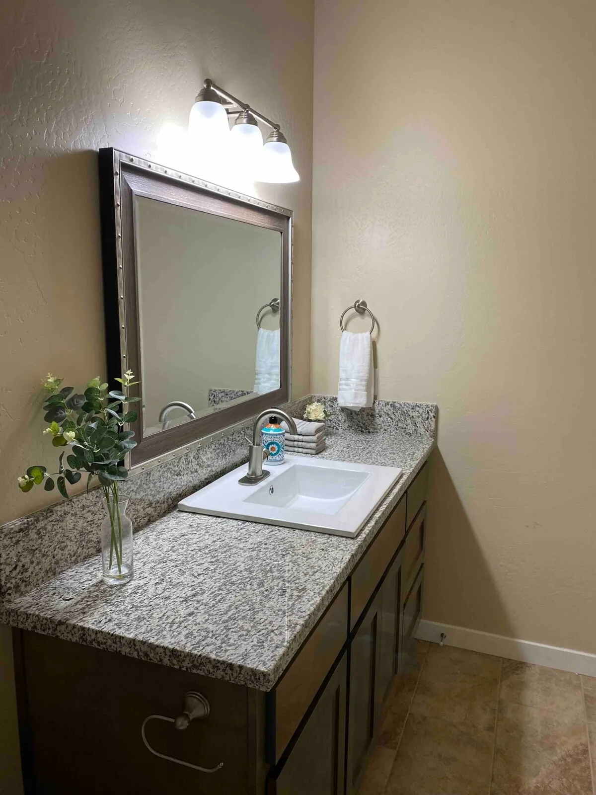 A sparkling, modern bathroom with a granite countertop, large mirror, sink, decorative plants, and neatly arranged towels. The space feels clean, fresh, and perfectly suited for moments of self-care and relaxation after a busy day.