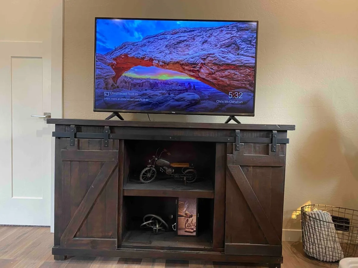 This interior scene highlights a comfortable living area featuring a large television atop a rustic cabinet, surrounded by decorative items. The setup suggests a spot for relaxation, entertainment, and socializing after a workday.