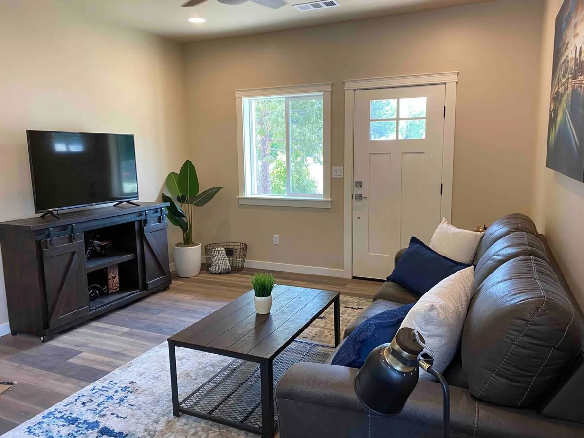 This image captures the heart of the living area, showcasing a plush sofa, a stylish coffee table, a modern television, a large window letting in natural light, and the front door. The arrangement emphasizes comfort and connectivity, with cozy seating and entertainment amenities at the forefront. The visible entryway and streaming-friendly setup reflect the 'fresh start' and 'living comfort' themes mentioned in the section.