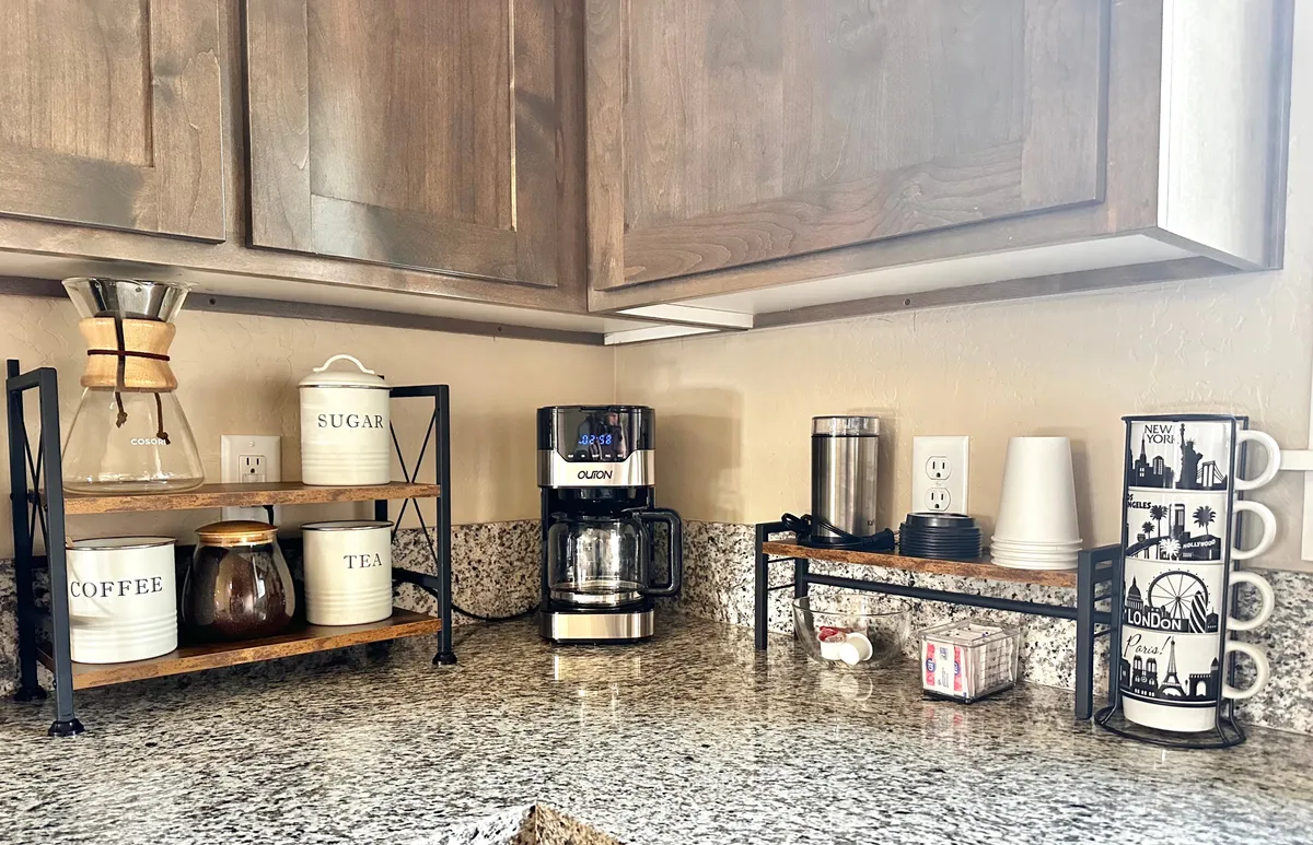 A well-appointed coffee nook with a modern coffee maker, sugar and tea jars, and a collection of travel-themed mugs. The setup creates a sense of warmth and hospitality, inviting guests to linger and share stories over hot beverages.