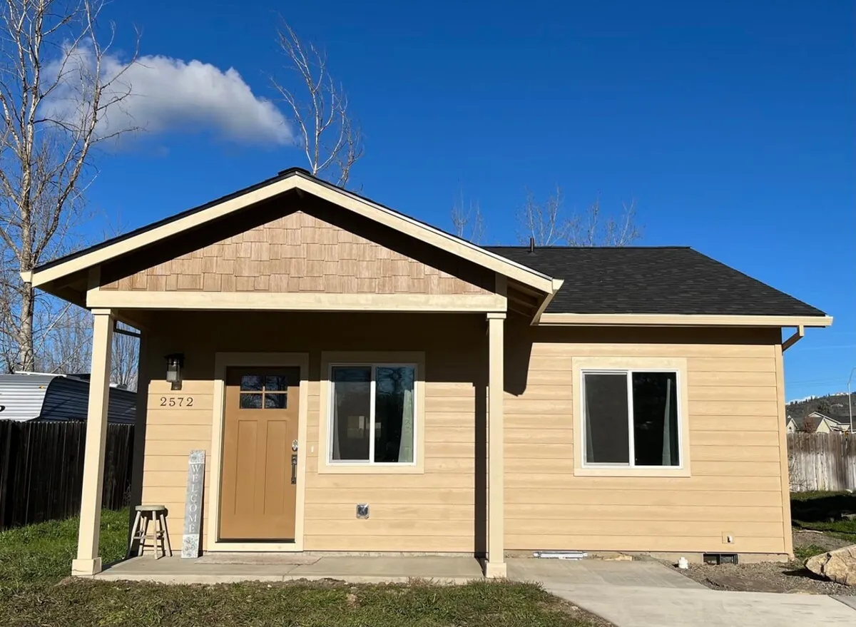 An exterior view of the cottage's front door, classic windows, and welcoming porch framed by a tidy yard. The scene radiates a sense of security and new beginnings, inviting guests to step inside the pristine, untouched interiors beyond.