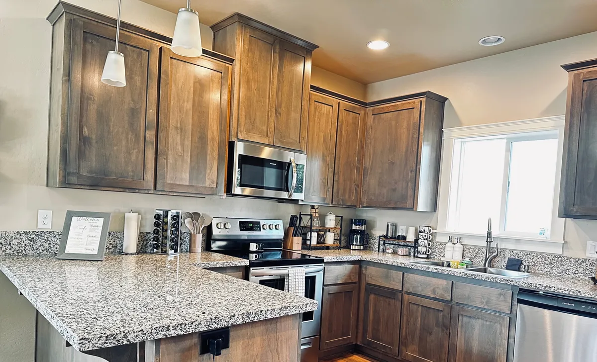 A modern kitchen scene with a central granite island, stainless steel appliances, and wooden cabinets. The layout invites both cooking and socializing, with space for guests or family to gather around the island, emphasizing a communal atmosphere.