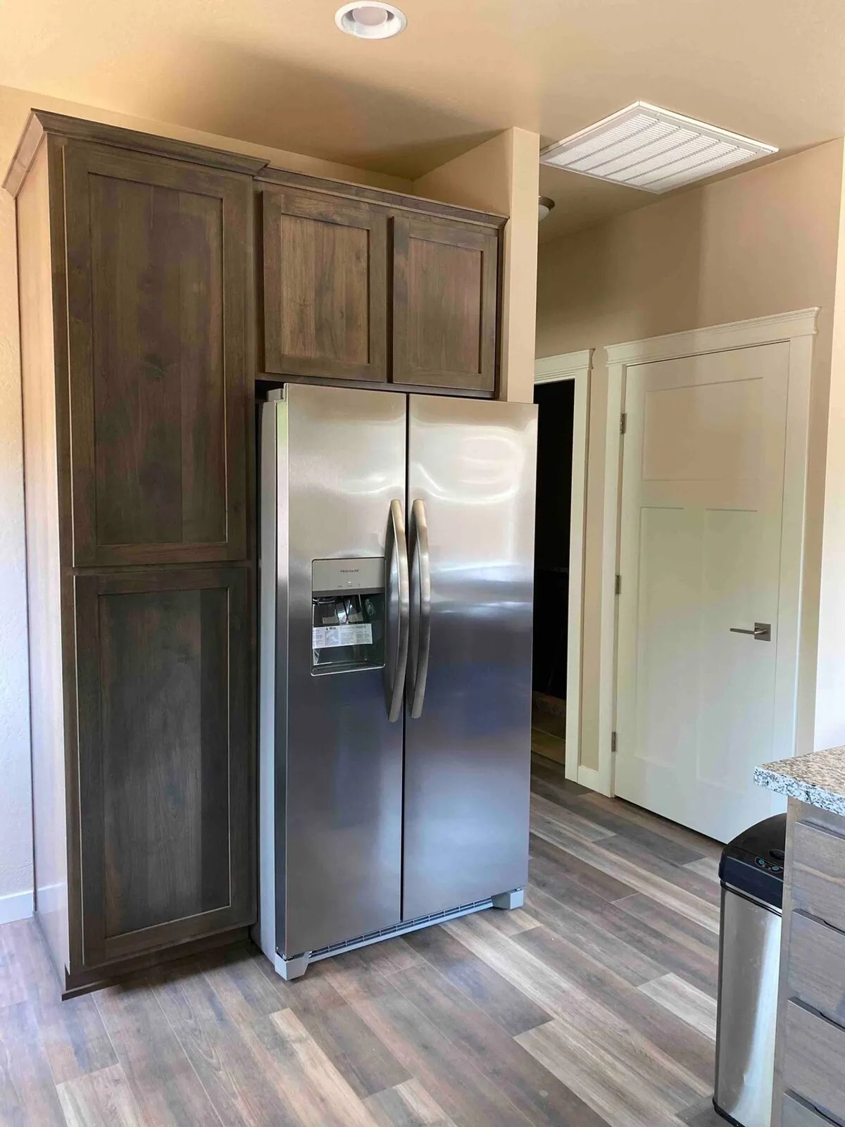 A modern kitchen with stainless steel refrigerator, wooden cabinets, and a spacious granite countertop. The scene is bright and practical, indicating ample space for quick meal preparation or casual dining.