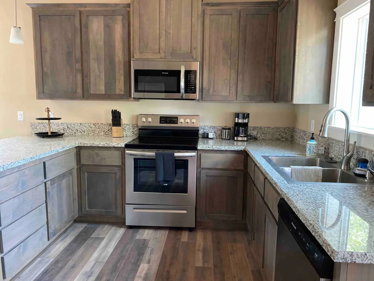 This image showcases a modern kitchen with granite countertops, stainless steel appliances, and wooden cabinetry. The spacious counters and open layout hint at a warm, communal atmosphere ideal for preparing family meals or snacks after a day out.